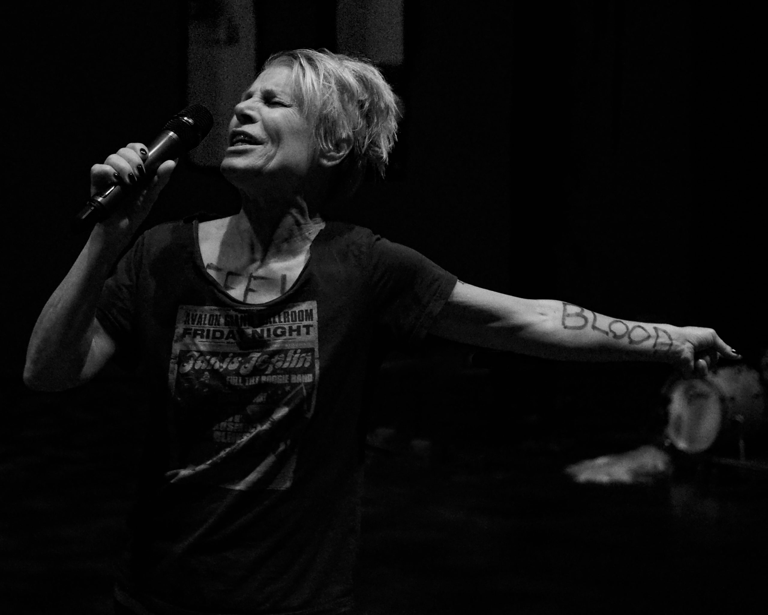 Katie Duck seen on stage with a microphone and the word "BLOOD" written on her forearm.